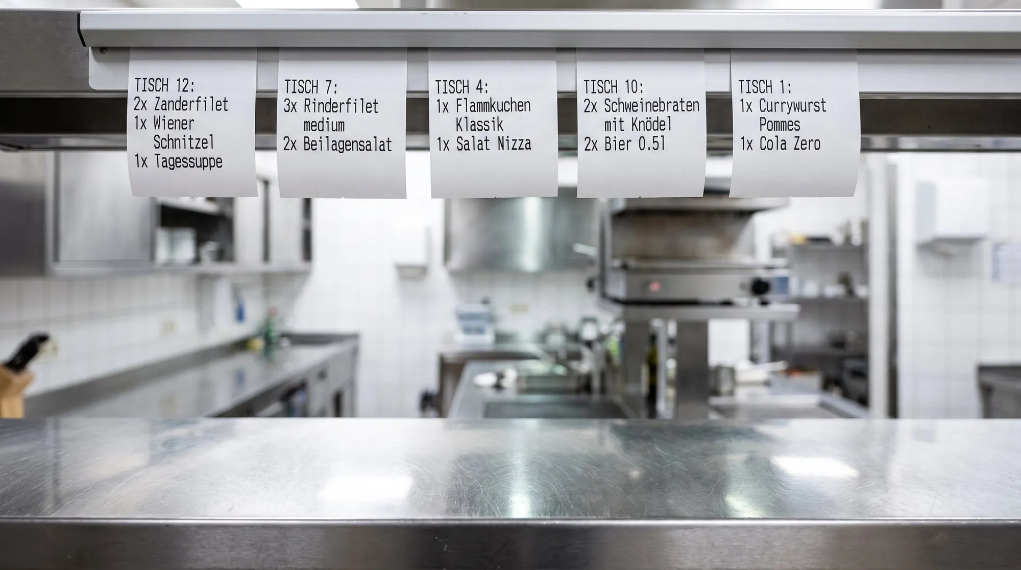 Ticket rail with order slips above the pass of a restaurant kitchen
